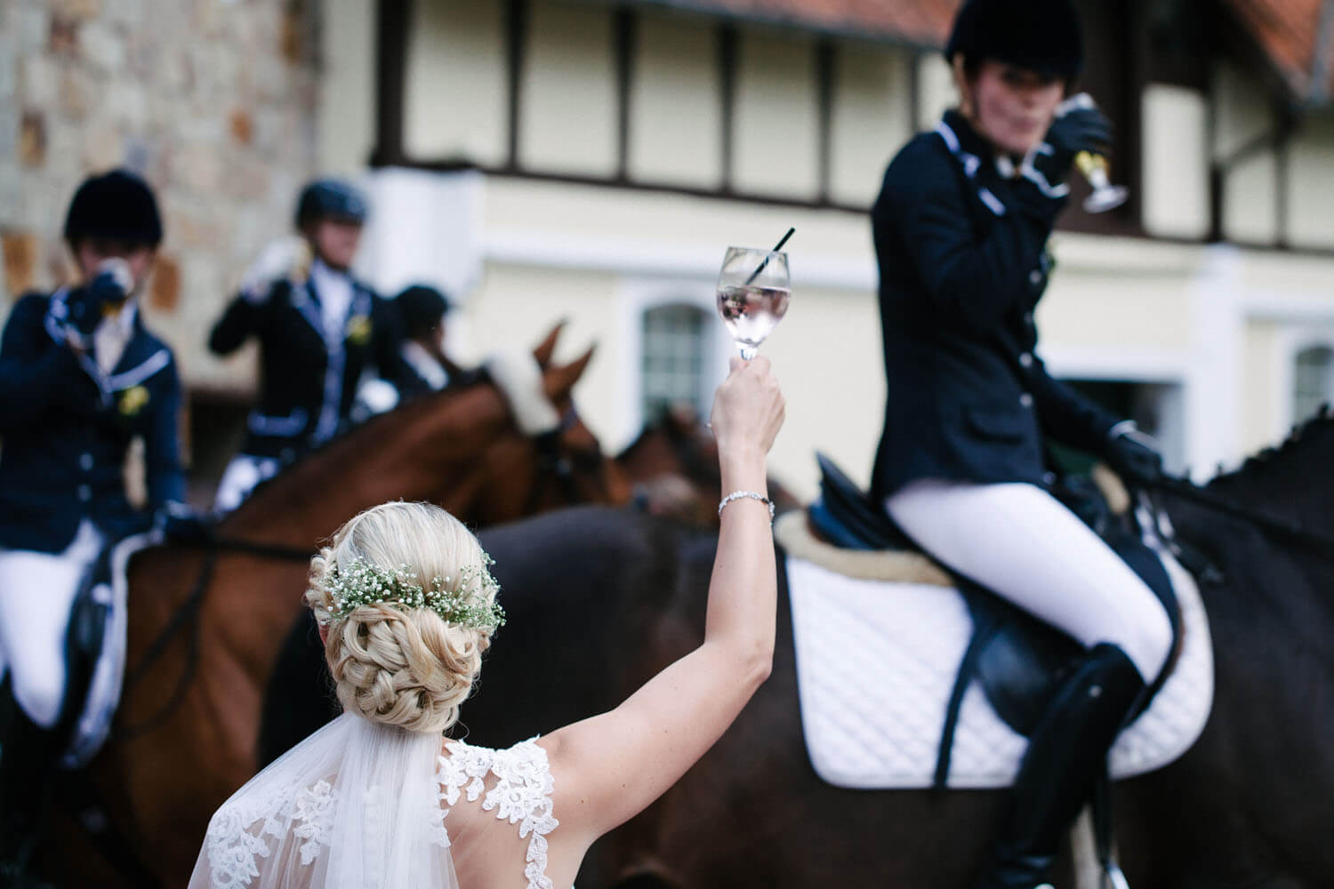 Braut prostet ihren Freundinnen auf Pferden im Hintergrund zu.